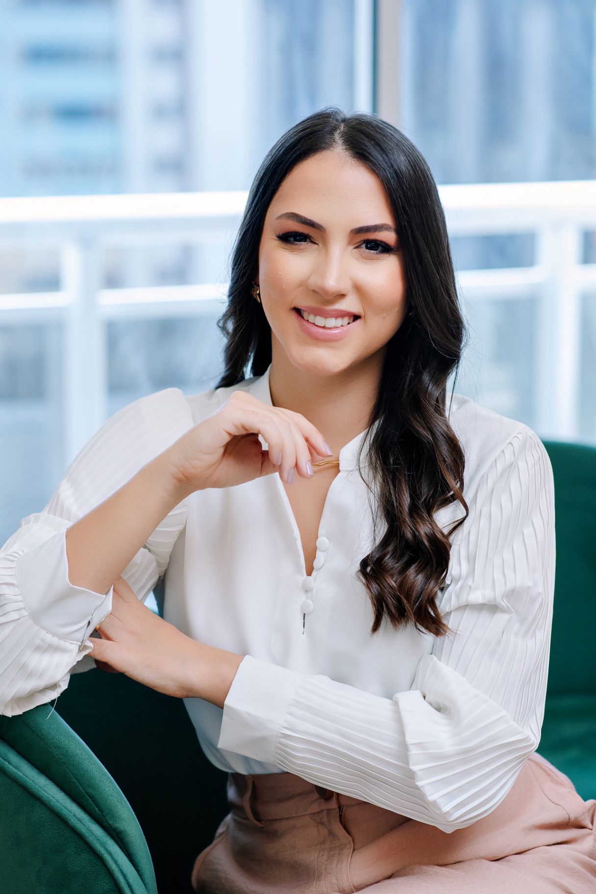 Dra. Thaís Alexandrino sorrindo, sentada em poltrona verde